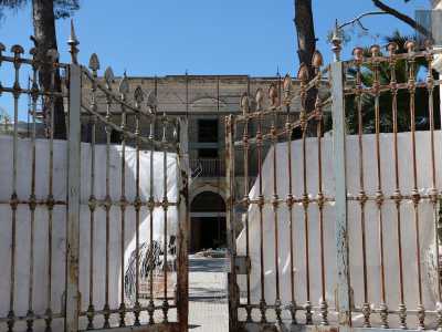 Lo stabile, di colore bianco, � preceduto da un cancello arrugginito che d� accesso a un vialetto